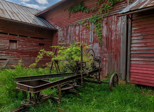 Old rusted farm equipment abandoned next to old barn in rural central Virginia