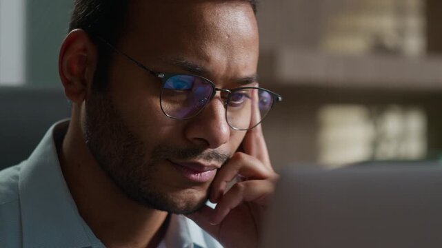 Pensive Indian American male business man reading bad news laptop indoors office thoughtful worker businessman thinking concerned problem computer solution worry anxiety difficulties failure bankrupt