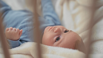 Baby boy lying in a studio crib on a soft blanket, eyes open and tiny hands moving while looking up through crib bars  serenity bonding comfort. © Krakenimages.com