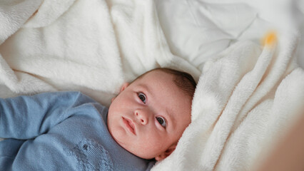 Baby boy lying on white blanket in bed reaches hand toward a hanging mobile above his face  calm curiosity. © Krakenimages.com