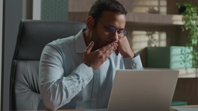 Tired Indian Arabian business man yawning in office bored with computer laptop work evening deadline exhausted businessman manager fatigued no energy overworked napping after online job stress burnout