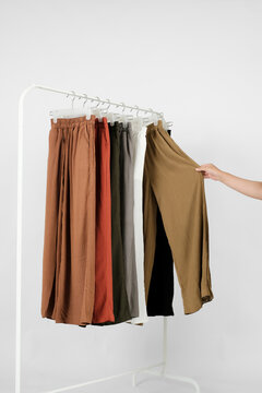 Female hand choosing comfortable khaki crinkle culottes pants from a colorful clothing rack against a white background. Retail shopping and fashion concept.