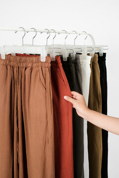 Detail shot of a customer's hand touching the pocket of trendy brick red crinkle culottes hanging on a white clothing rack. Casual women's fashion shopping.