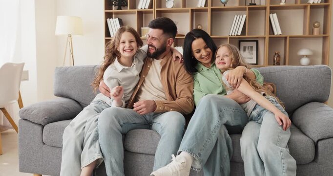 Family parents father mother daughters hug together. They sit smiling at home on a cozy sofa, enjoying bonding and genuine connection in a bright room. Clear concept of loving family.