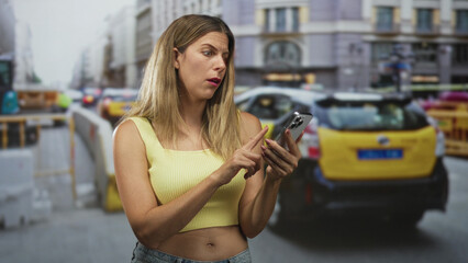 Naklejka premium Woman checking smartphone with midriff exposed, standing on street by construction barriers and taxi; frustration delay problem.