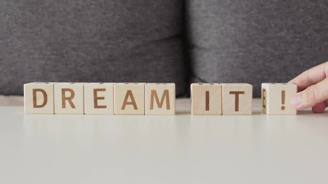 motivational phrase dream it !, laying out  by hand from letters on wooden cubes, slow motion

