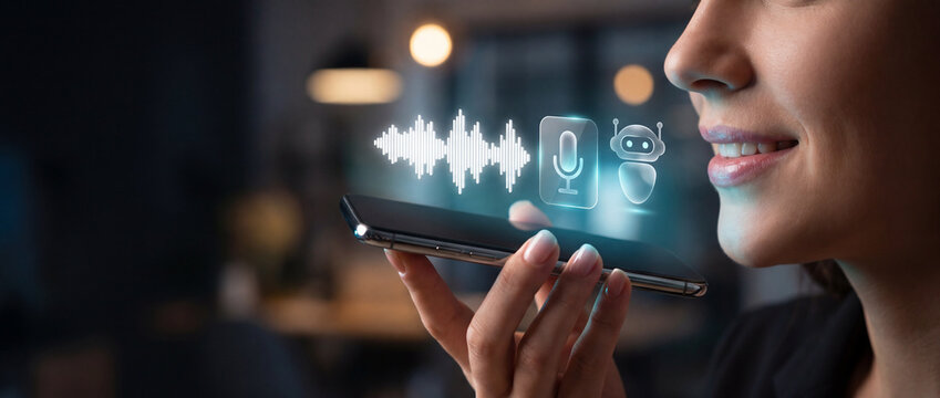 Close-up of a woman speaking into a smartphone displaying a voice waveform, microphone icon, and chatbot interface, suggesting AI assistant interaction and voice command technology in a dimly lit
