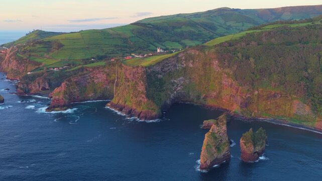 Aerial view of Miradouro dos Caimbros cliffs with green hills and sea stacks along the rugged coastline in Cedros, Acores, Portugal.