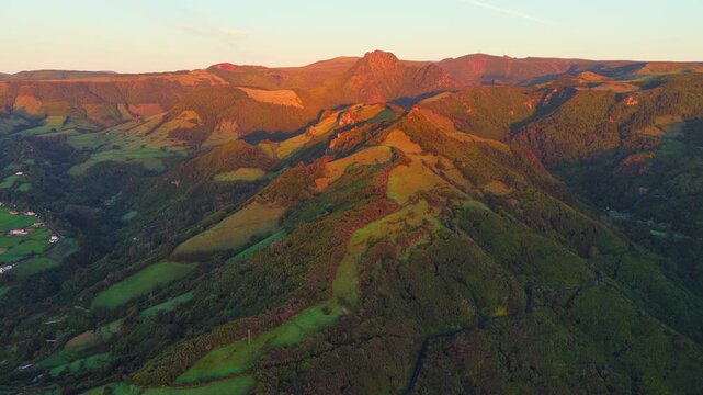 Aerial view of Miradouro dos Caimbros overlooking lush green volcanic hills and valleys at sunset in Cedros, Acores, Portugal.