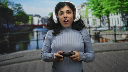 Arab woman with headset holding game controller on street by an amsterdam canal  urban gaming concentration. © Krakenimages.com