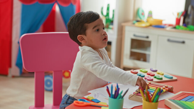 Little boy reaches for maraca with his hand on a red table in a playroom building; curiosity learning exploration.