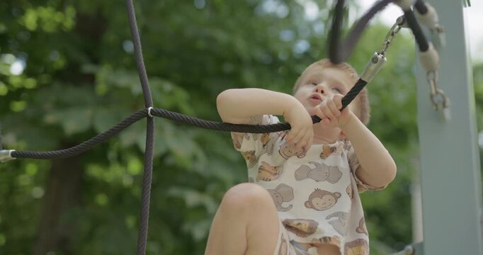 Little toddler boy climbing on playground equipment in summer park