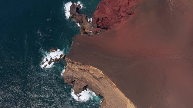 Aerial view of Capelinhos volcanic cliffs with dark red and black soil meeting the deep blue Atlantic Ocean in Capelo, Azores, Portugal.