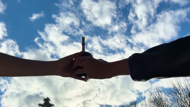 Close up of two hands sharing traditional yerba mate, Argentine drink against a blue sky with clouds background