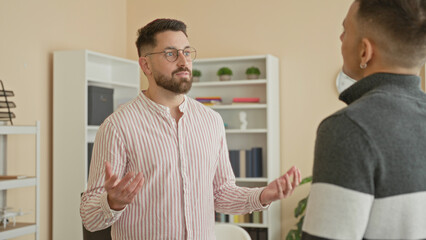 Man speaking with hand gestures and wearing glasses to a coworker in an office building, bookshelves visible and hands emphasized during discussion  teamwork focus. © Krakenimages.com