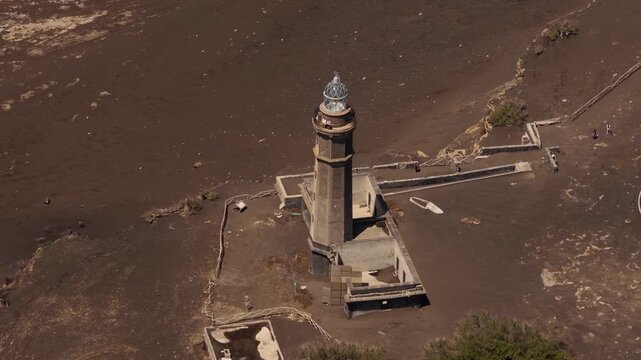 Aerial view of the historic Capelinhos lighthouse standing amidst the dark volcanic landscape of the coast in Capelo, Azores, Portugal.