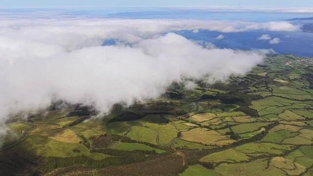 Aerial view of green patchwork fields and rolling hills under clouds in Horta, Azores, Portugal.