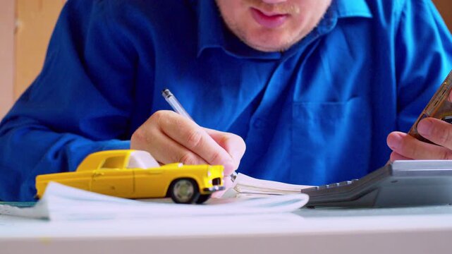 Businessman doing math with office calculator and smartphone close up. Car insurance agent checking data at desk.Hands focus, shallow depth of field, bright natural daylight.