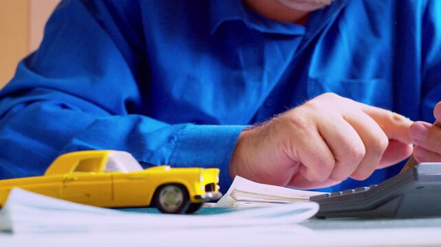 Slow zoom. Agent hands using calculator and holding smartphone. Car insurance office desk with yellow toy car. Close up, selective focus, shallow depth of field, natural daylight scene