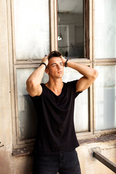 Young man posing with hands in hair by window