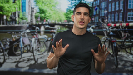 Fototapeta premium Man with hands palms out gesturing on amsterdam street beside parked bicycles and canal walkway; caution.