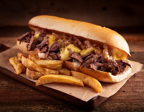 classic cheesesteak featuring steak cheese onions served on toasted hoagie roll with side of french fries on rustic table