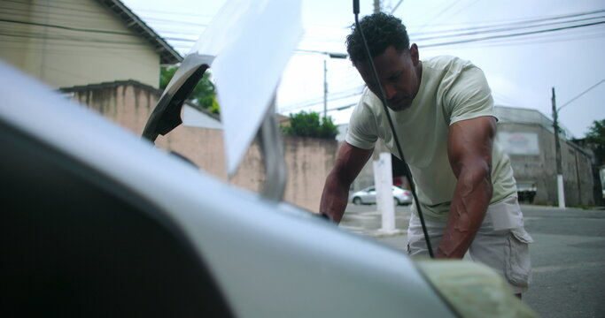 Man frustrated while examining broken car on the street, holding head in stress, showcasing struggle and problem-solving during a difficult situation in an urban environment