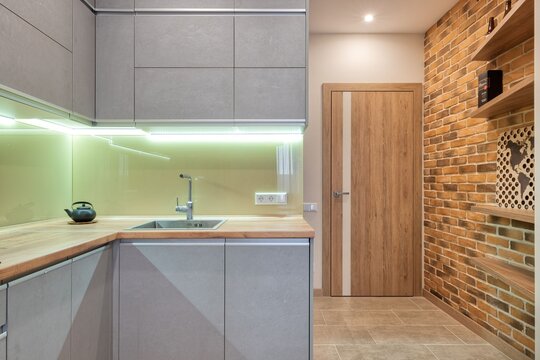 Modern Minimalist Gray Kitchen Interior Design with Wooden Countertop LED Backlight and Rustic Exposed Brick Accent Wall Contemporary Apartment Loft Photo