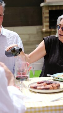 Woman pouring red wine for a friend during a cheerful outdoor summer lunch party in the garden