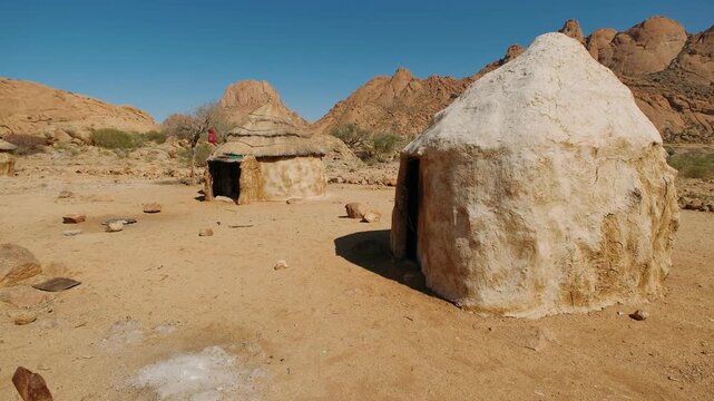 Traditional himba huts in a namibia village with a mountain desert landscape in the background, damaraland