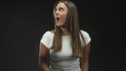 Naklejka premium Woman brunette in white tshirt singing with mouth open and glancing to the right in studio; curiosity.
