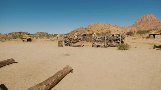 Traditional african himba village with huts and a wooden fence in the dry namibian landscape near spitzkoppe mountain