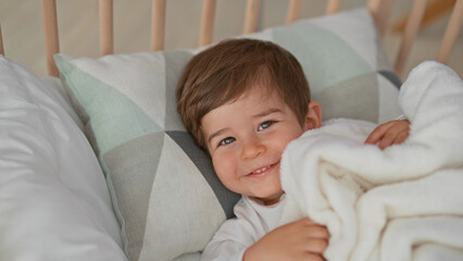 Little boy clutching a white blanket in a wooden crib, hand gripping blanket, resting on a pillow inside a building nursery room  contentment. © Krakenimages.com