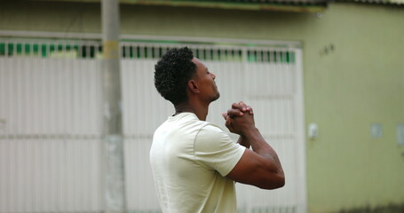 Fototapeta premium Man smiling gently with clasped hands, looking skyward, a moment of hope and gratitude, symbolizing faith and devotion, connecting deeply with spirituality in an urban setting