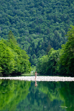Solo female traveler standing on a river islet in the Kolpa valley, showcasing eco friendly tourism, untouched forests and relaxing summer vacations