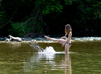Fototapeta premium Woman splashing water playfully in a mountain river, capturing carefree summer holidays, adventure travel and refreshing natural experiences outdoors