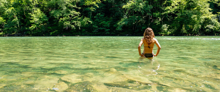 Woman immersed in clear river waters during a sustainable summer escape, representing freedom, environmental tourism and countryside relaxation