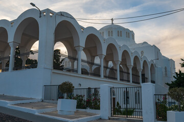 Exterior view of whitewashed arches and domed church with iron fence in Santorini, Greece, under a soft evening sky. © Andrei Tomas