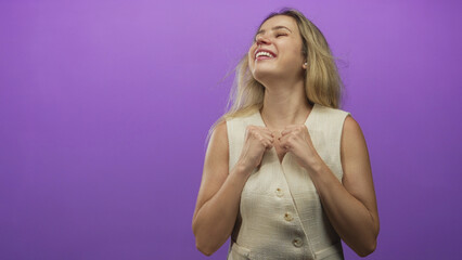 Obraz premium Woman smiling with fists raised and exposed arms wearing a sleeveless vest in a purple studio; joy empowerment.
