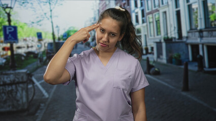 Fototapeta premium Young latina woman in lilac scrubs with slumped shoulders and closed eyes on city street; fatigue duty.