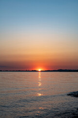 Obraz premium Beautiful sunset over Lake Constance captured from the Austrian shore, showing the vibrant sun setting behind the distant horizon with warm golden reflections on the calm water surface