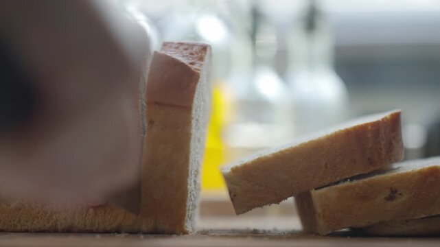 Hand slicing bread with knife, cutting thick pieces from a loaf. Concept of breakfast preparation and toast recipe