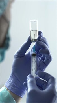 Medical gloves doctor or nurse filling syringe with medicine liquid from glass vial vertical B roll close up shot in 4K Ultra HD footage.

