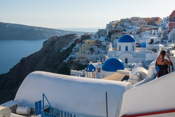 Santorini, Greece - 07.06.2026: Visitors walk along whitewashed rooftops overlooking iconic blue-domed churches and the Aegean Sea at sunset. © Andrei Tomas