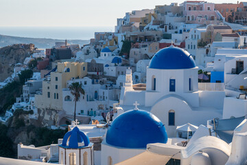 Panoramic view of whitewashed buildings and iconic blue domes in Oia, Santorini, Greece, with Aegean Sea on the horizon at golden hour. © Andrei Tomas