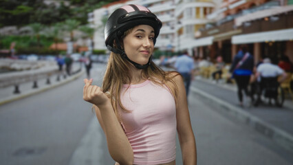 Fototapeta premium Young woman showing pinched fingers gesture with hand on city street, wearing pink tank and helmet; confident attitude.