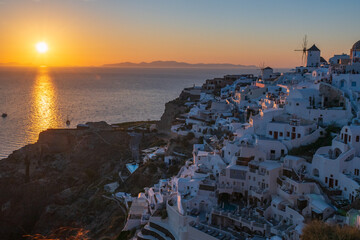 Golden sunset reflecting on the Aegean Sea beside whitewashed houses and windmills on the Oia caldera cliffs in Santorini. © Andrei Tomas