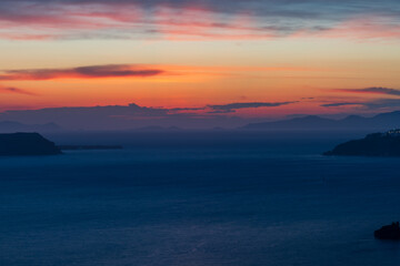 Fototapeta premium Vibrant orange and purple dusk sky above the Aegean Sea and distant island silhouettes, tranquil seascape from Santorini.