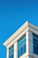 Obraz premium Corner of a light-colored building with blue windows against a clear sky