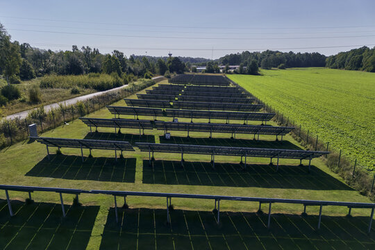 Aerial view of rows of solar panels in a small solar park situated under high voltage power lines in a rural landscape, Svenstorp, Blekinge County, Sweden.